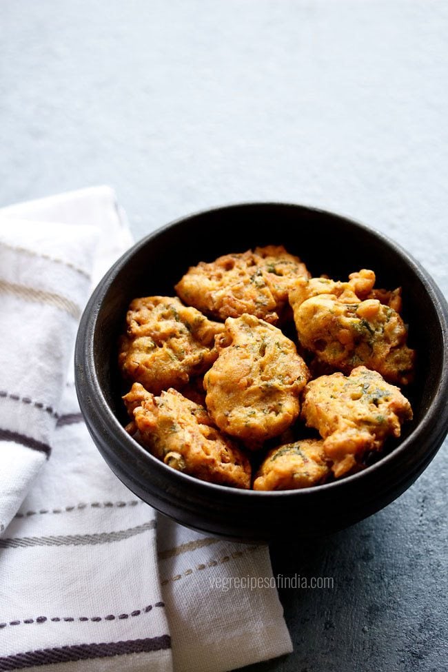 mix vegetable pakora in a black wooden bowl placed next to a white striped kitchen linen