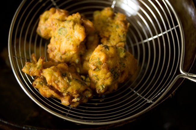 crisp, golden fried mixed vegetable pakora in a steel spider-spoon 