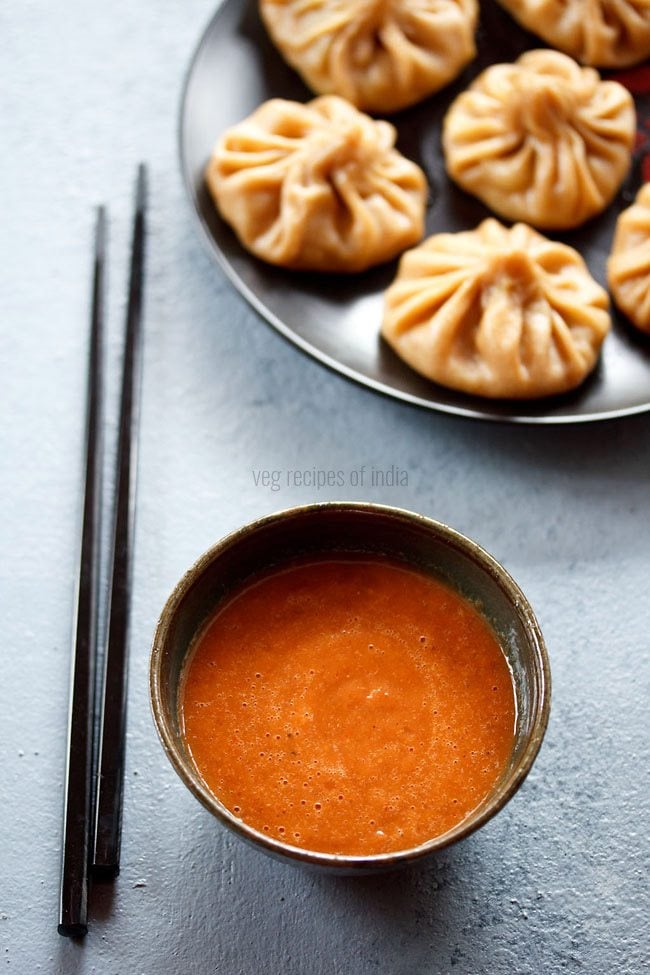 momos chutney served in a bowl with chopsticks on the side and momos kept on a platter above. 