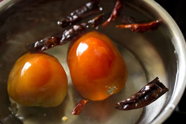 tomatoes and dried red chilies added to hot water in pan. 