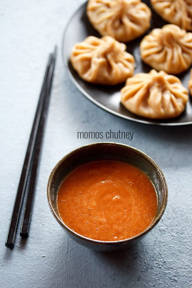 momos chutney served in a bowl with chopsticks on the side, momos on a platter above and text layovers.