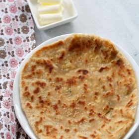 paneer kulcha served on a white plate with a side of butter in a small bowl.
