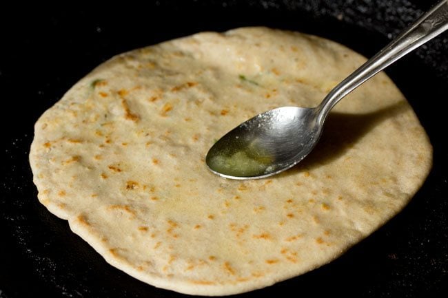 spreading some ghee on the paneer kulcha while being roasted. 