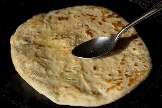 spreading some ghee on the paneer kulcha while being roasted. 