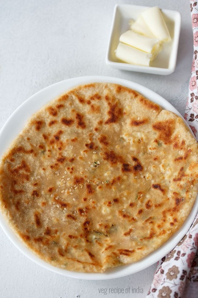 paneer kulcha served on a white plate with a side of butter in a small bowl. 