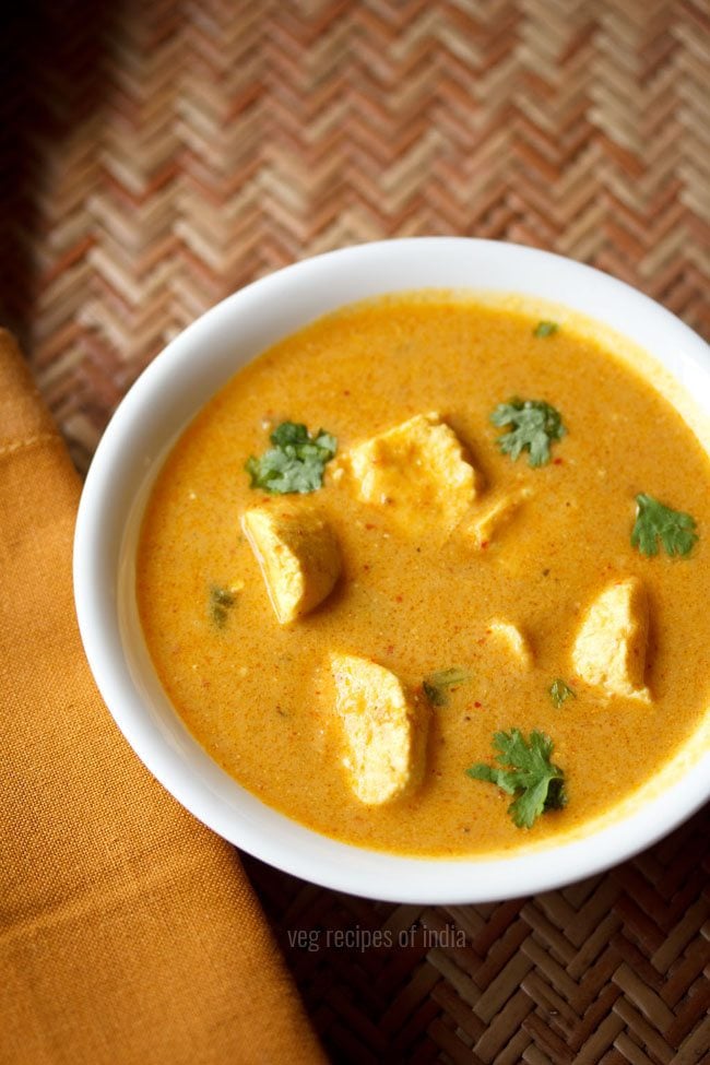 white bowl of paneer curry garnished with fresh cilantro leaves on an orange tablescape