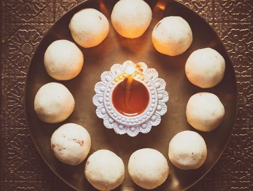 rava ladoo in a circle with lit earthen lamp in center on a bronze plate.