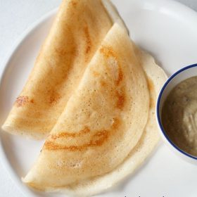 sabudana dosa folded and served on a white plate with a bowl of chutney kept on the left side.