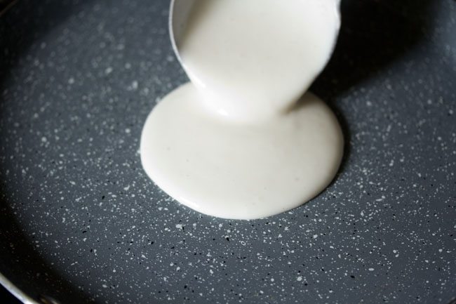 pouring dosa batter in the center of a non stick pan. 