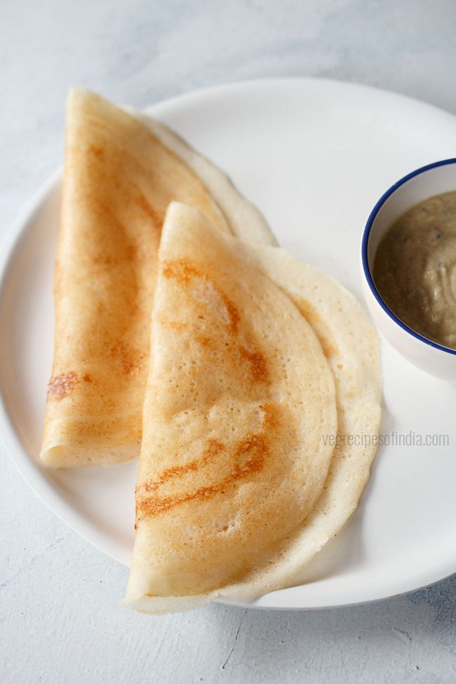 sabudana dosa folded and served on a white plate with a bowl of chutney kept on the left side and text layovers. 