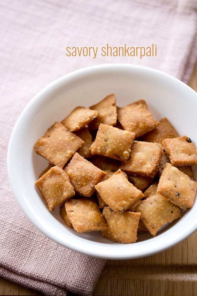 top shot of savory shankarpali filled in white bowl on a light pink linen with text layovers