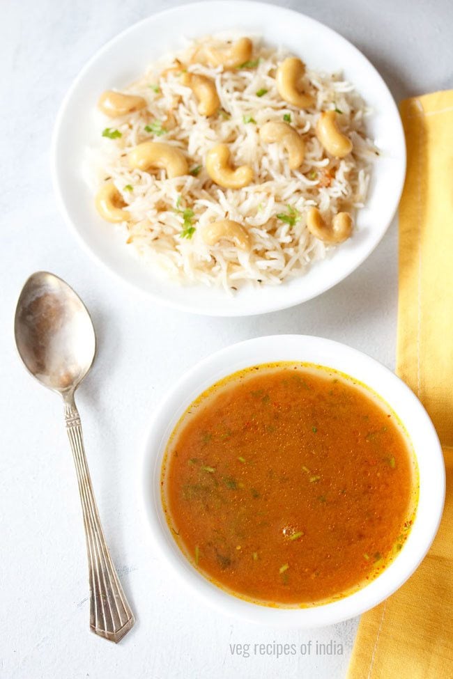 tomato shorba served in a white bowl with a spoon kept on the left side, a bowl of cashew pulao kept on the top side and text layover.