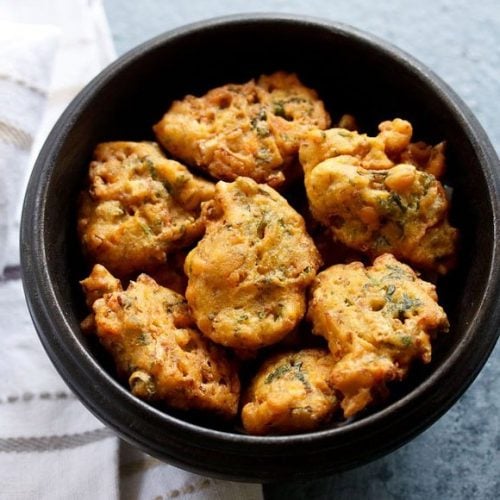 vegetable pakora in a black wooden bowl placed next to a white striped kitchen linen