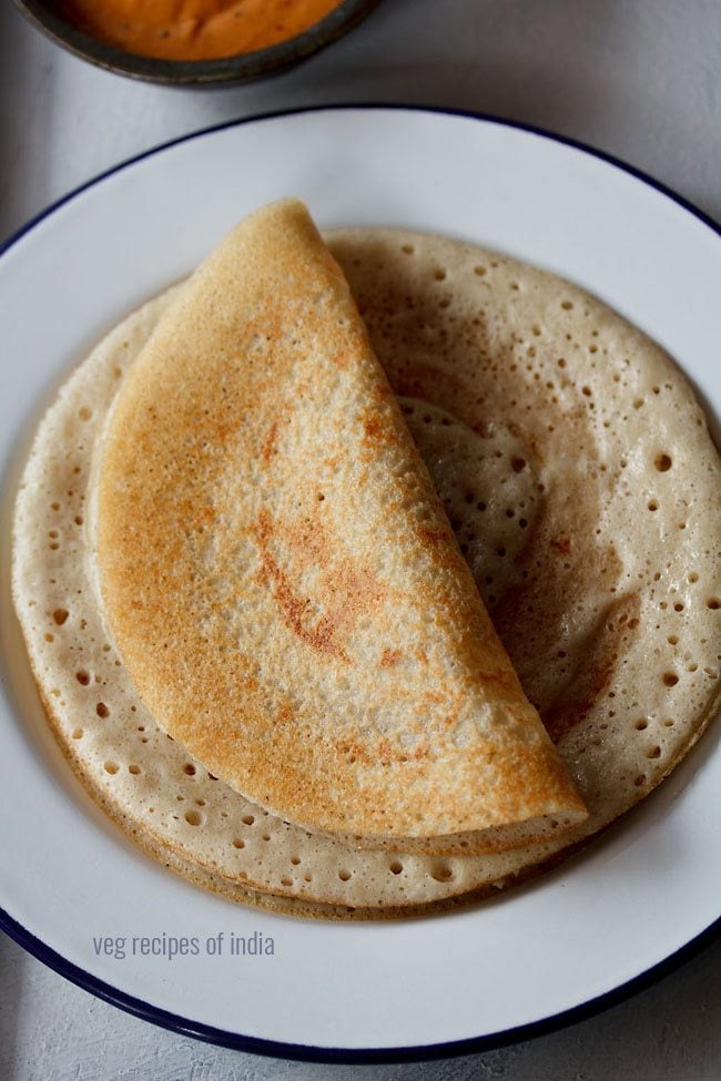 vendhaya dosa served folded on top of another dosa on a blue rimmed white with text layovers. 