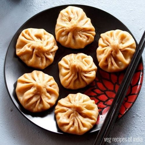 wheat momos arranged on a black plate with black chopsticks.