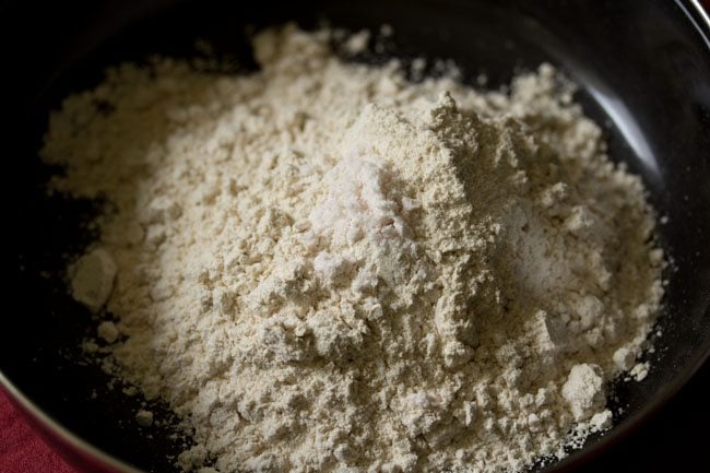 whole wheat flour and salt added to a black mixing bowl for wheat momos recipe.