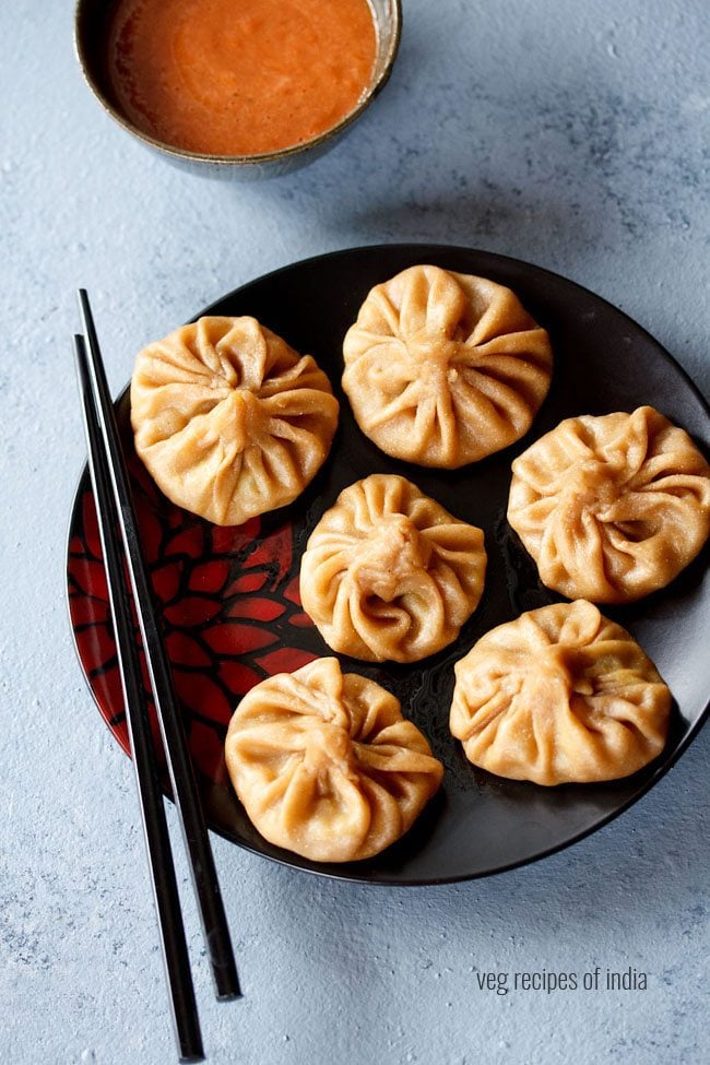 wheat momos arranged on a black plate with black chopsticks kept on the left side. 