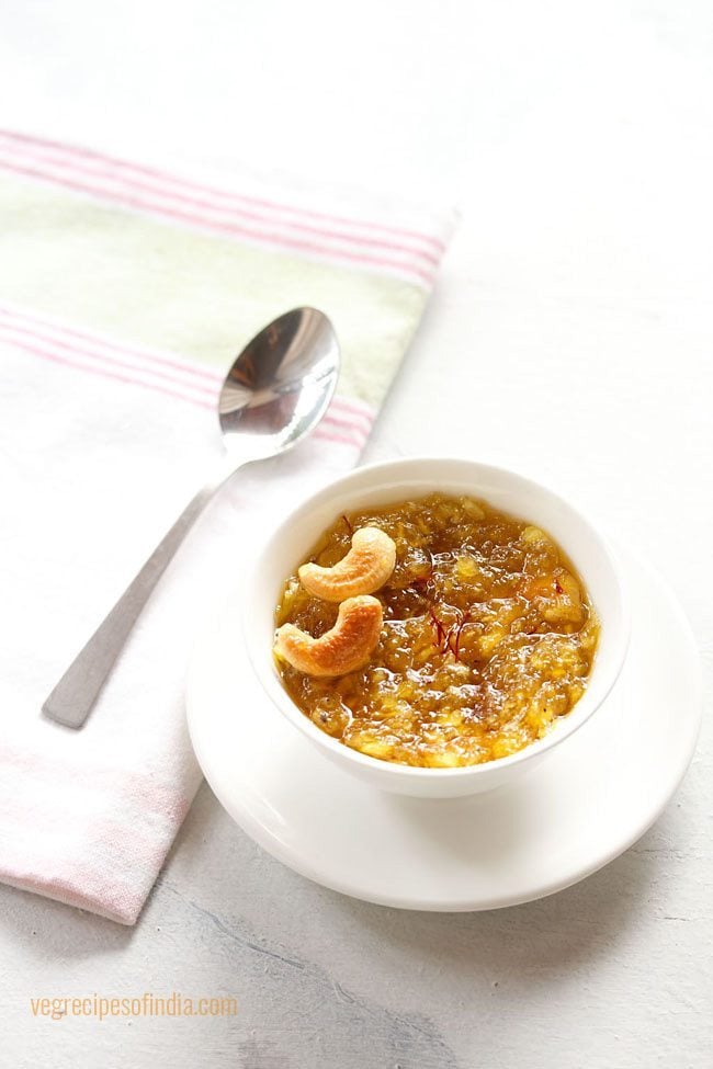 kashi halwa garnished with fried cashews served in a white bowl on a white plate with a spoon kept on the left side and text layover. 