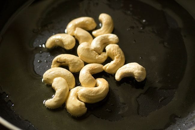 cashews added in hot ghee in a heavy pan for making white pumpkin halwa. 