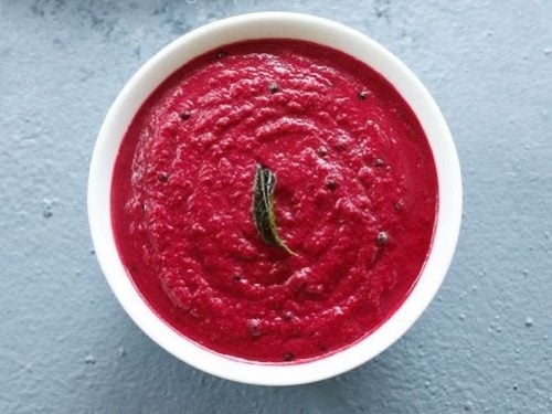 overhead shot of beetroot chutney in white bowl on a light grey blue board with text layovers