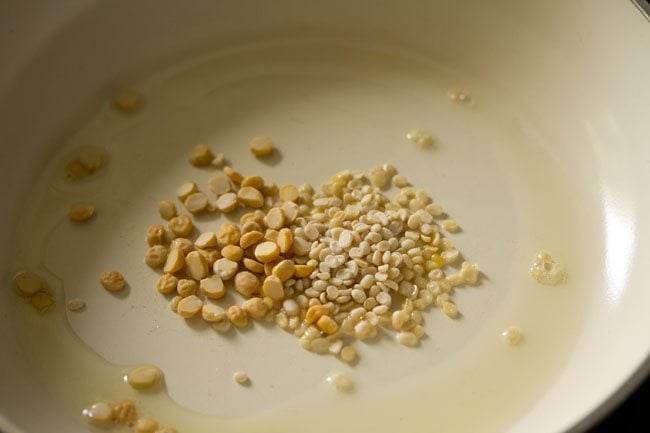 sesame oil, urad dal and chana dal in a cream colored pan