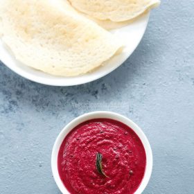 overhead shot of beetroot chutney in white bowl on a light grey blue board with dosa in a white plate on top