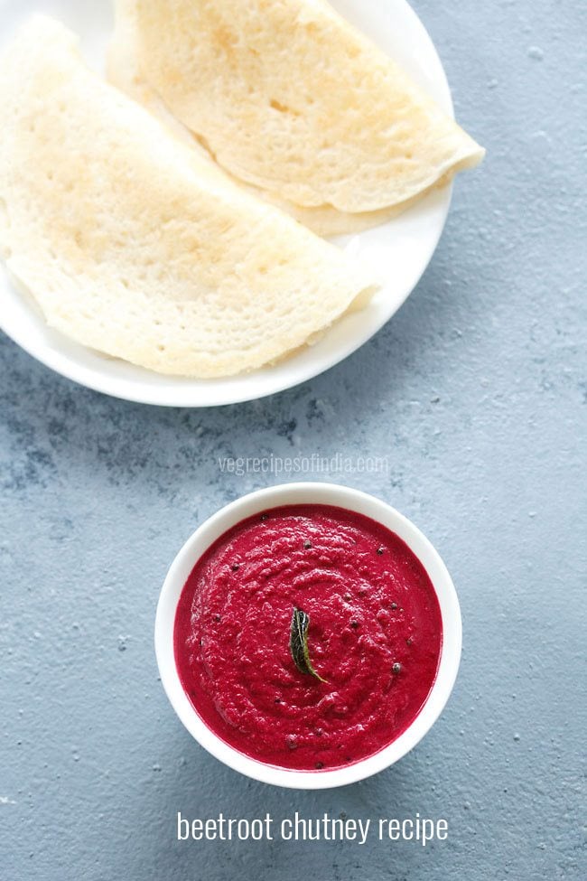 Overhead shot of beetroot chutney in a white bowl on a light gray blue board with dosa on a white plate on top