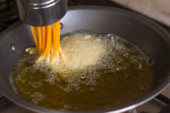 pressing sev maker into hot oil to fry besan sev. 