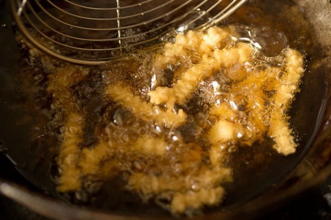 turning over butter murukku with a slotted spoon to fry evenly. 