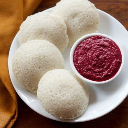 instant idli on a white plate with a white bowl of beetroot chutney