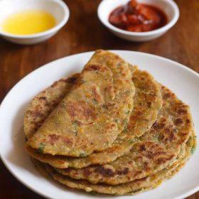 kaddu ka paratha served on a white plate with one paratha folded and kept on top and a small bowl of butter and pickle kept in the background and text layover.