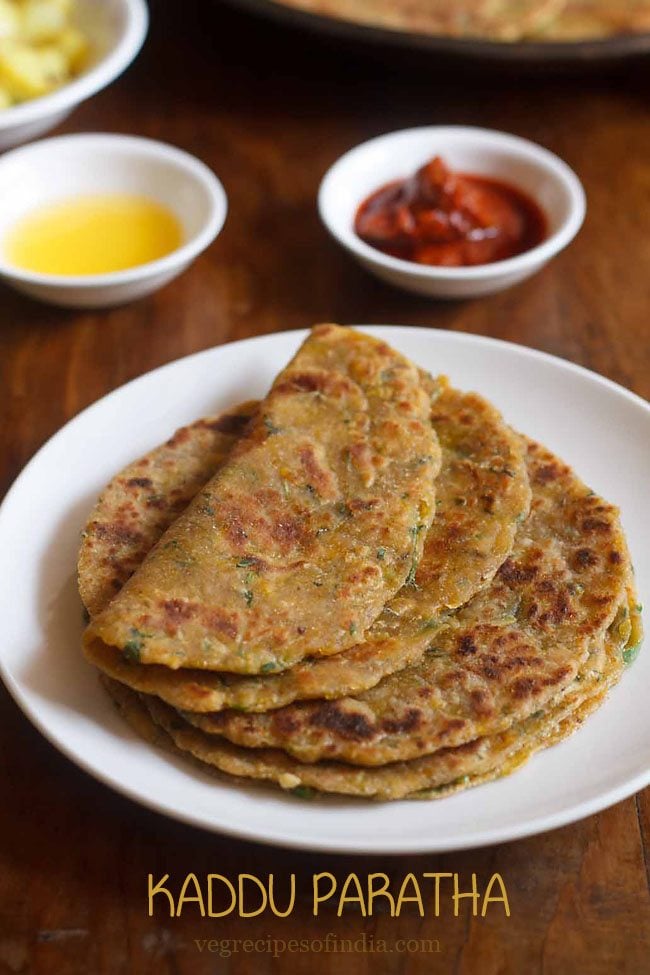 kaddu ka paratha served on a white plate with one paratha folded and kept on top and a small bowl of butter and pickle kept in the background and text layover.