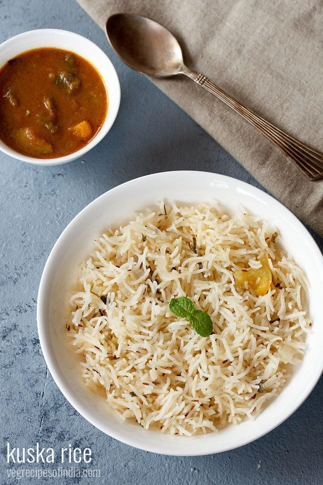 kuska rice garnished with a mint sprig and served in a white plate with a bowl of curry on the top left side.