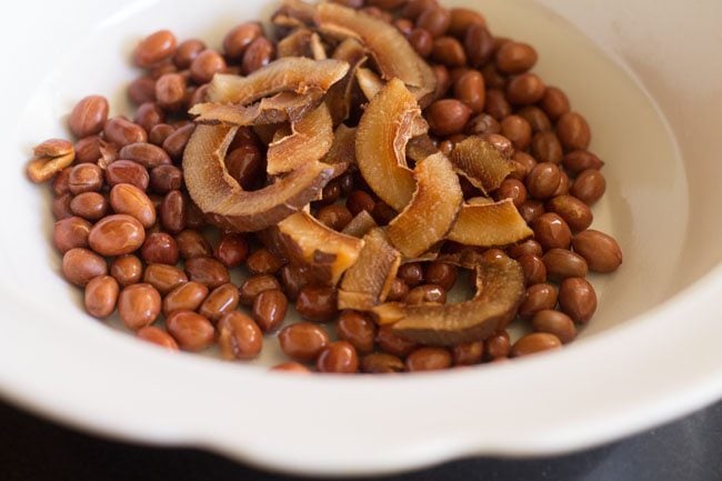 golden brown coconut slices on fried peanuts in white bowl