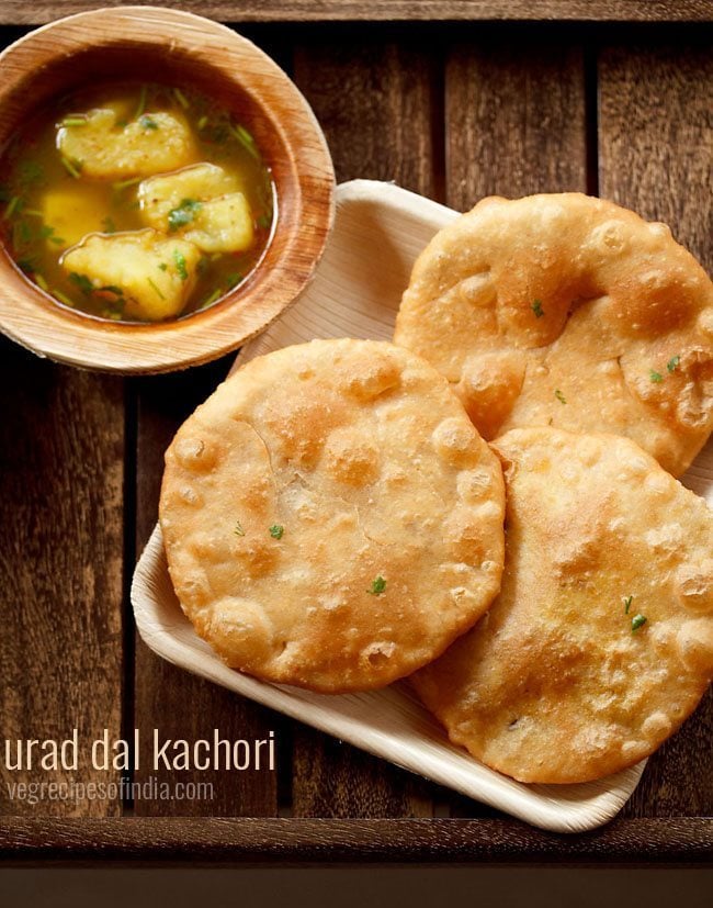 urad dal kachori served on a white platter with a bowl of aloo rasedar on the left side and text layovers.