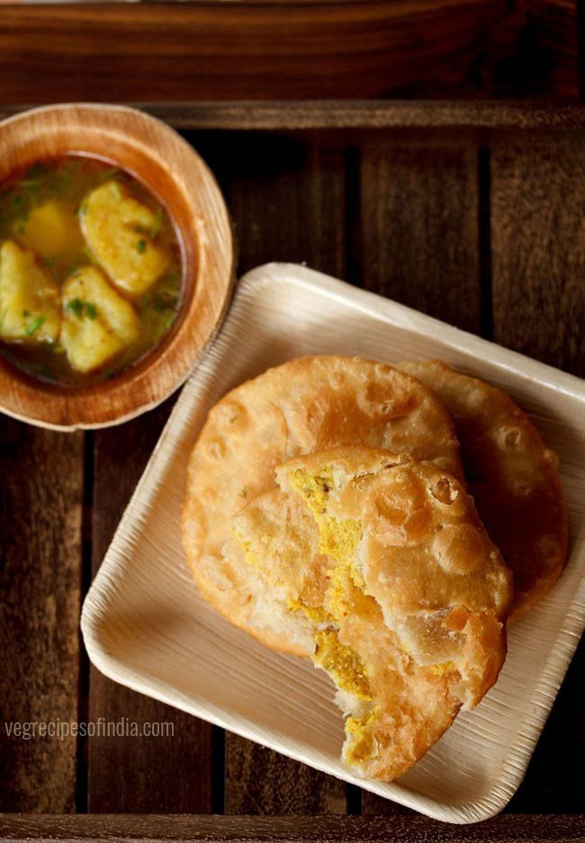 urad dal kachori served on a white platter with a broken kachori on top, a bowl of aloo rasedar on the left side and text layover. 