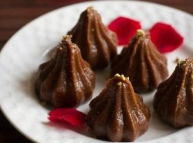 closeup shot of chocolate modak served on a white plate garnished crumbled pistachio and decorated with red rose petals.