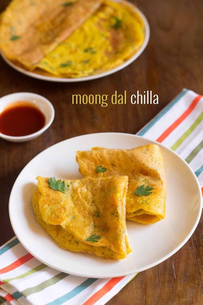 moong dal chilla folded and garnished with coriander leaves, served on white plate with a small bowl of tomato ketchup kept on the top left side and text layover.