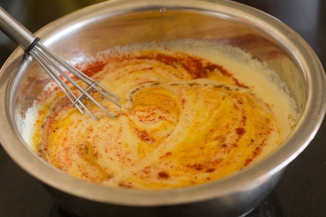 mixing the salt and spices in the moong dal batter with a wired whisk. 