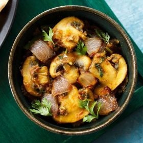 mushroom do pyaza garnished with cilantro sprigs in a dark olive green ceramic bowl on a dark green board