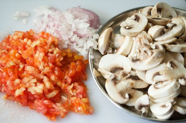 finely chopped onions, tomatoes and chopped mushrooms on a white cutting board