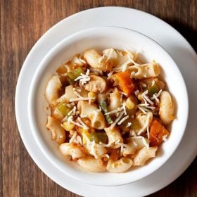 red sauce pasta garnished with grated cheese and served in a white bowl kept on a white plate.