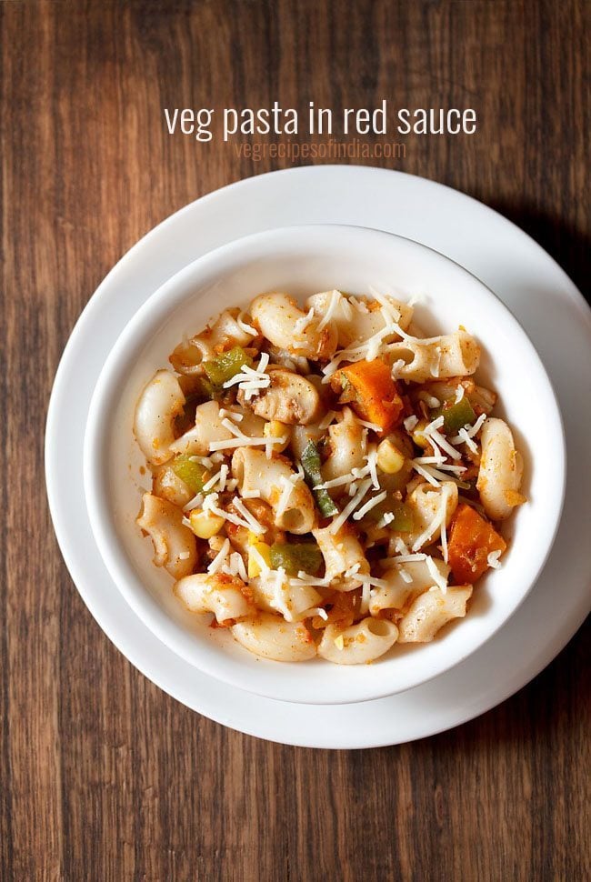 red sauce pasta garnished with grated cheese and served in a white bowl kept on a white plate.