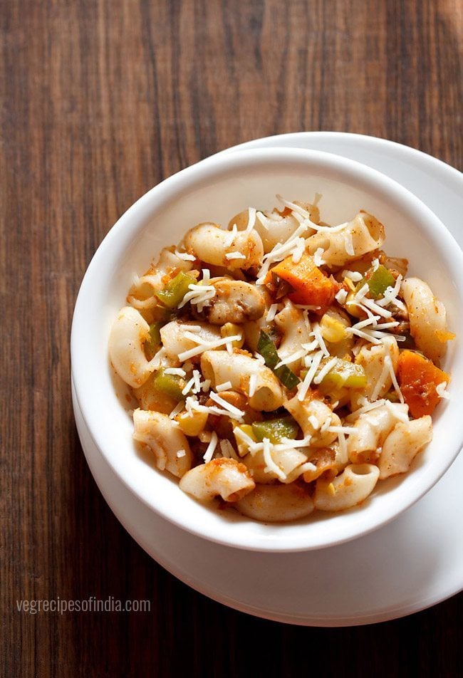 red sauce pasta garnished with grated cheese and served in a white bowl kept on a white plate. 