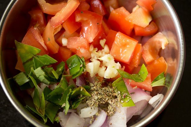 adding chopped garlic, chopped basil leaves and dried oregano to chopped vegetables 