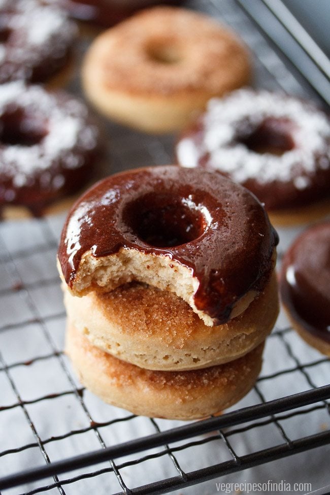 chocolate donut with a bite placed on top of two donuts