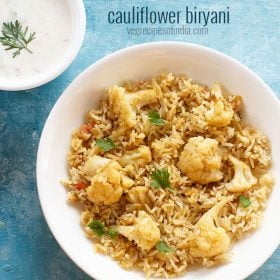 cauliflower biryani garnished with coriander leaves and served in a white bowl with a bowl of raita kept in the top left side and text layovers.