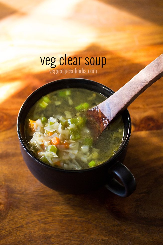 vegetable soup in a black bowl with a wooden soup spoon with some veggies on it in the bowl on a wooden board