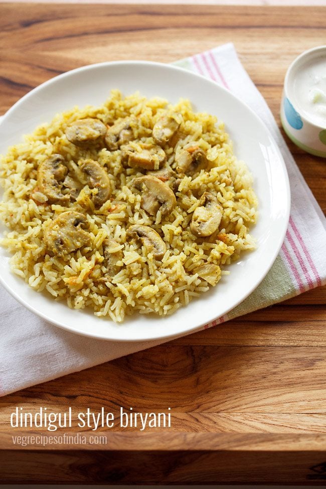 dindigul biryani served on a white plate with a small bowl of raita kept on the right side.