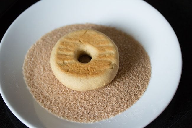 donut with buttered side placed touching cinnamon and sugar mixture 